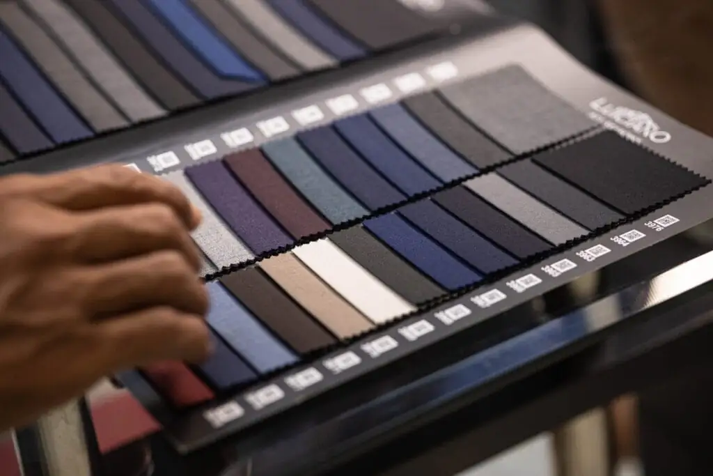 Hand turning the pages of a swatch book of navy and grey suiting samples