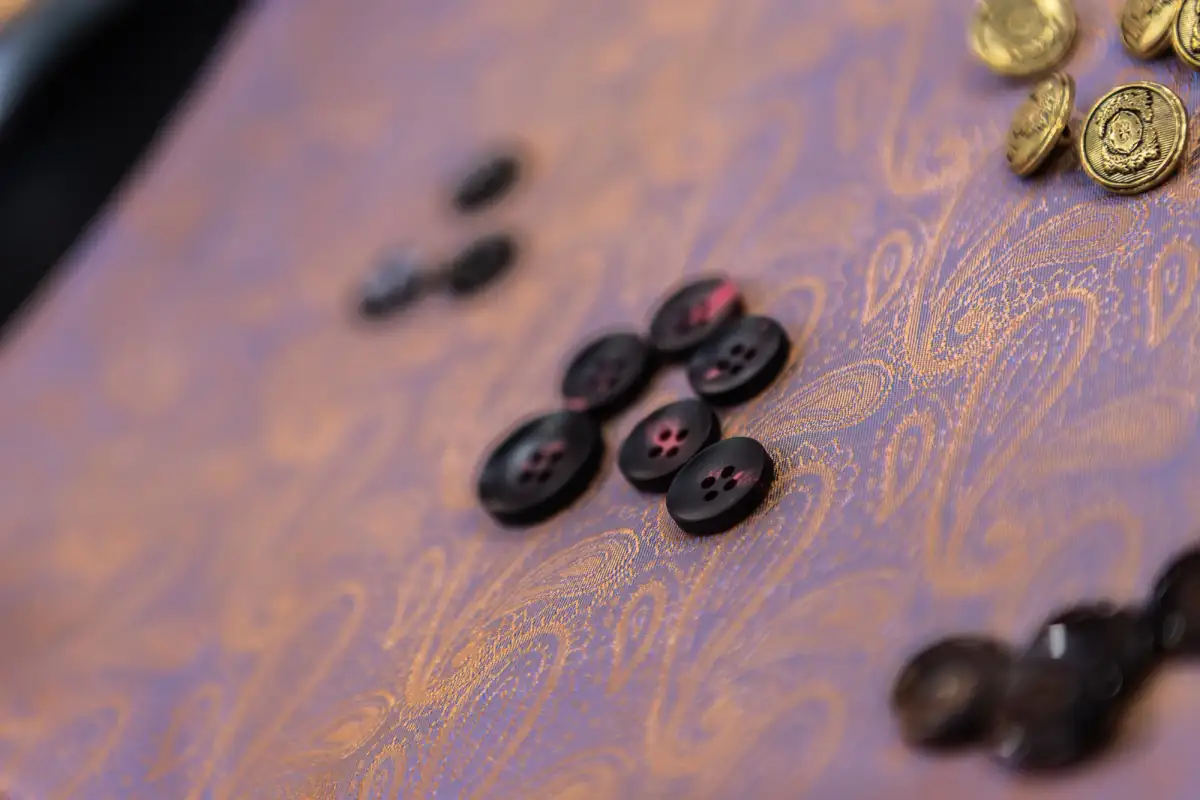 Dark horn suit buttons and gilt blazer buttons laid out on gold paisley silk