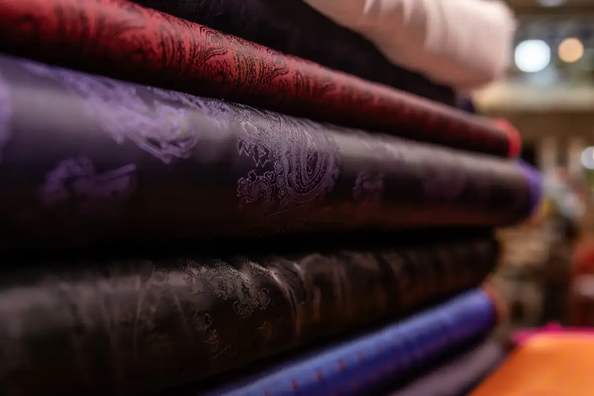 Stacked bolts of paisley-jacquard silk lining in red, purple and bronze on the shop shelf